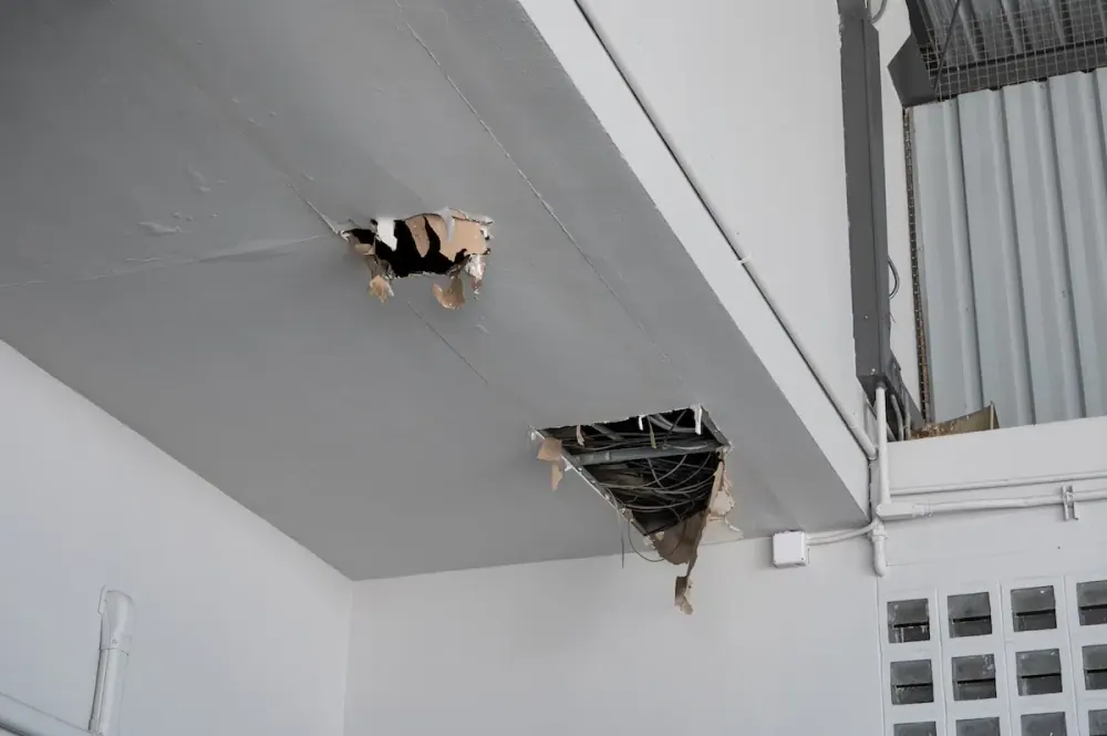 Ceiling with a collapsed drywall panel and exposed wiring caused by a roof leak