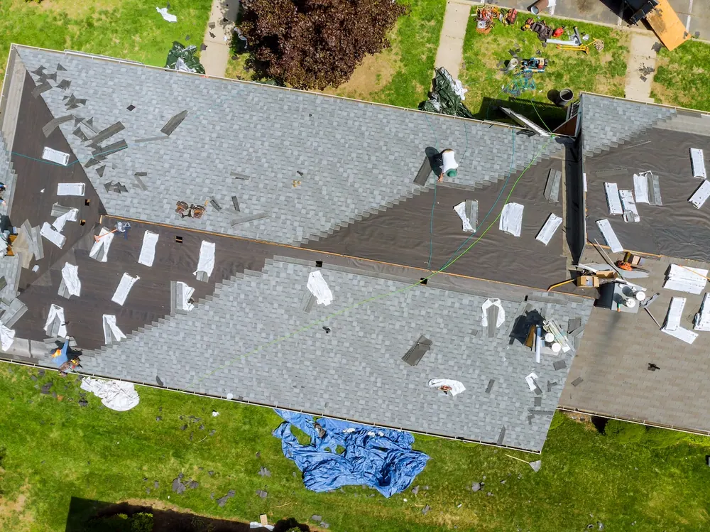 Aerial view of a roofer replacing storm-damaged shingles on a residential roof